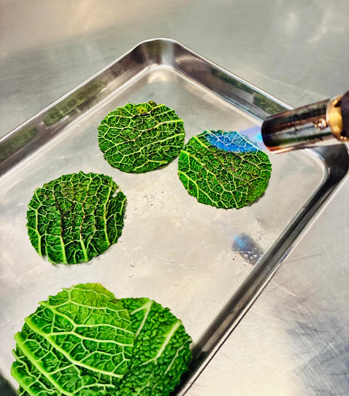 Préparation culinaire en cuisine avec feuille de chou travaillée au chalumeau